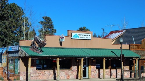 A rustic building with a green roof and a moose sculpture, featuring a sign for "Mountain View Donut Plus."