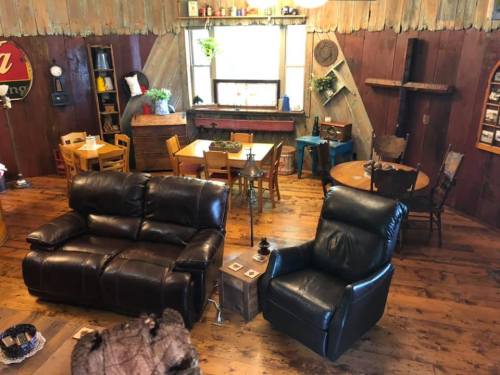 Cozy living room with leather sofas, wooden floors, and a rustic dining area featuring various tables and decor.
