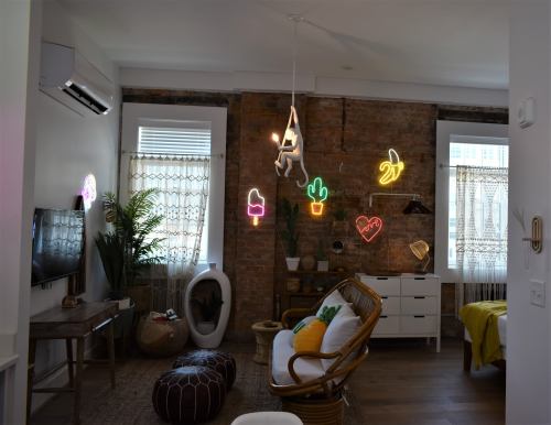 A cozy living room with a brick wall, neon lights, plants, and modern furniture, creating a vibrant atmosphere.