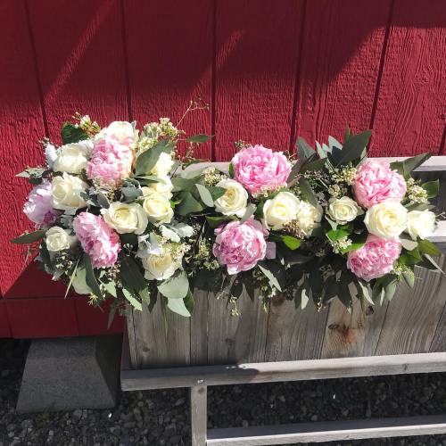 A vibrant arrangement of pink peonies and white roses with greenery, displayed against a red wooden background.