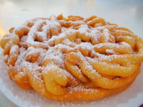 A golden-brown funnel cake dusted with powdered sugar, served on a white plate.