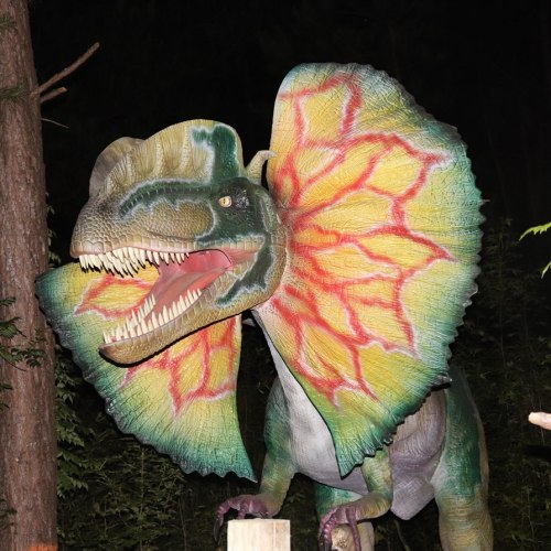 A colorful dinosaur statue with a large frill, set against a dark forest background.