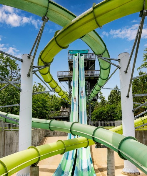 A vibrant water slide complex with twisting green tubes and a tall tower under a blue sky and trees.