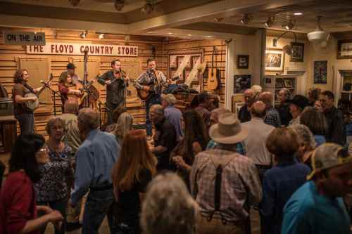 A lively bluegrass band performs on stage while a crowd dances in a cozy country store setting.