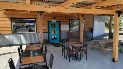 Outdoor seating area of a rustic restaurant with wooden beams, tables, and a bright blue door.