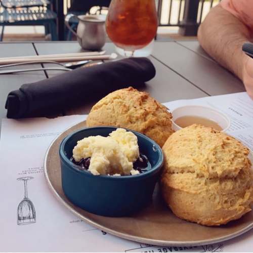 Two freshly baked biscuits on a plate, served with a small bowl of blueberry compote and a side of butter.