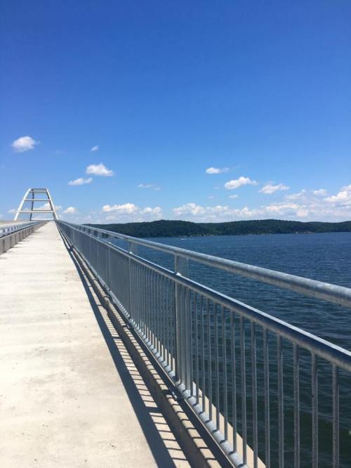A long pier extends over calm water, with a clear blue sky and distant hills in the background.