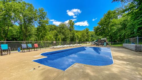 A clear blue pool surrounded by green trees and lounge chairs under a bright blue sky.