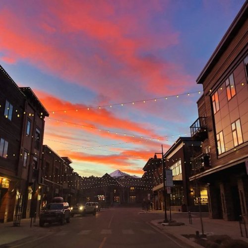 A vibrant sunset paints the sky in pink and orange over a charming street lined with shops and string lights.