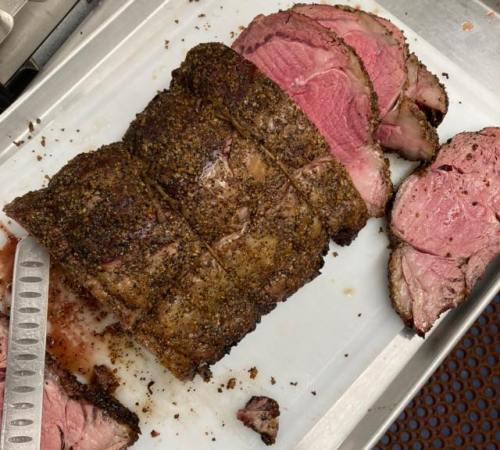 Sliced roast beef on a cutting board, showcasing a seasoned crust and pink interior.