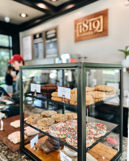A display case filled with various baked goods, including cookies and bars, in a cozy café setting.