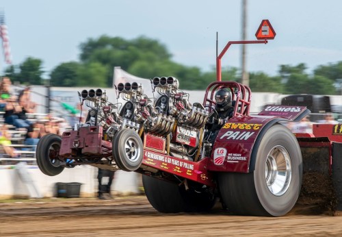 A modified tractor pulling vehicle lifts its front wheels during a competition, showcasing powerful engines and excitement.