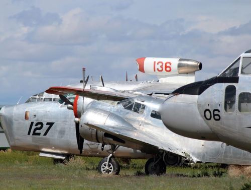 A row of vintage aircraft, including a silver plane with the number 127 and another with 136, against a cloudy sky.