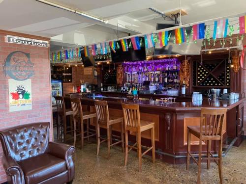A vibrant bar with colorful decorations, wooden stools, and a well-stocked counter under bright lights.