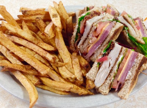A plate of crispy French fries next to a stacked sandwich with layers of meat, lettuce, and tomato on whole grain bread.