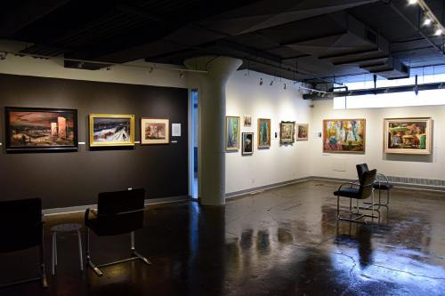 Art gallery interior featuring various framed paintings on the walls and seating in the foreground.