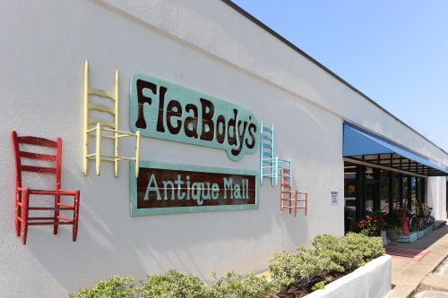Sign for FleaBody's Antique Mall with colorful chairs mounted on the wall, sunny day, and storefront visible.
