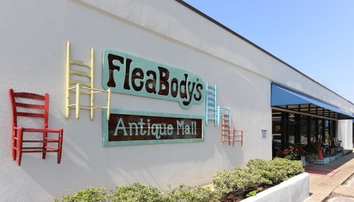 Exterior of FleaBody's Antique Mall, featuring colorful chairs on the wall and a bright blue awning.
