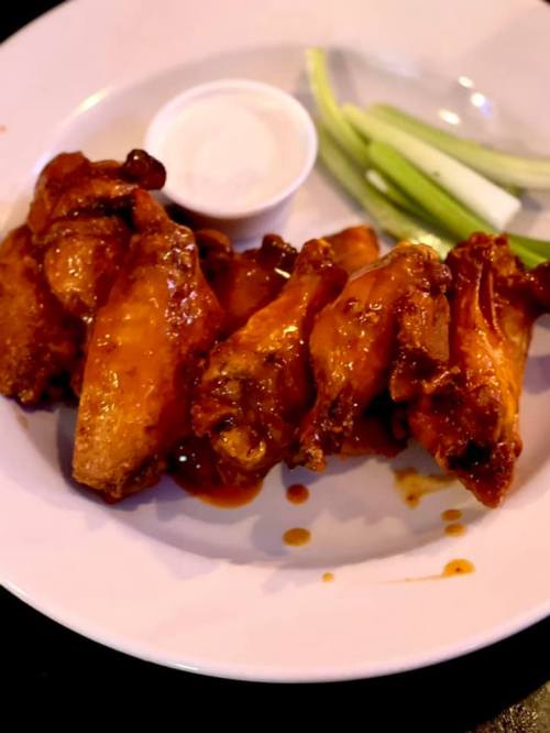 A plate of saucy chicken wings with a side of celery and a small cup of ranch dressing.