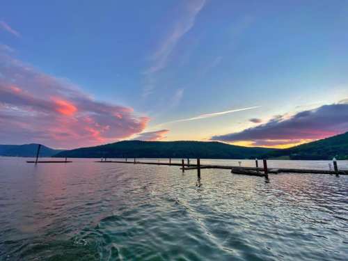 A serene lake at sunset, with colorful clouds reflecting on the water and a wooden pier extending into the distance.