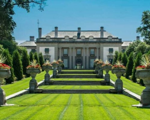 A grand mansion with a symmetrical garden featuring neatly trimmed lawns and decorative planters.