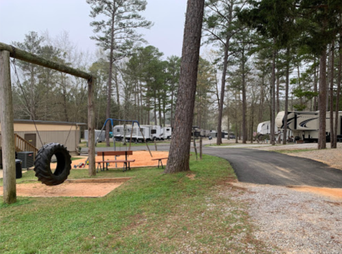 A campground with RVs lined up, a playground with a swing set, and a gravel path surrounded by trees.