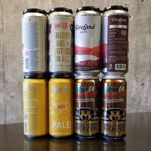 A collection of various beer cans stacked against a concrete wall, featuring colorful labels and different brands.