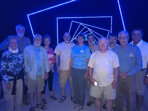 A group of people posing together in a dimly lit space with blue neon lights creating a geometric pattern.