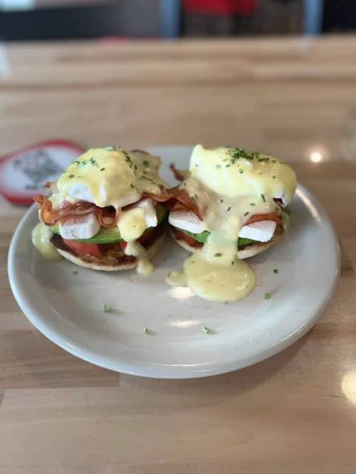 Two eggs Benedict on English muffins, topped with bacon and hollandaise sauce, garnished with chives on a white plate.