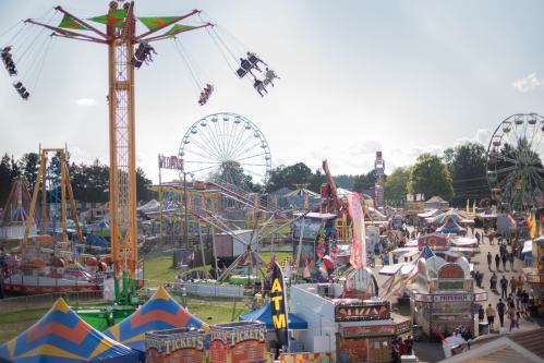 A vibrant carnival scene with rides, games, and colorful tents under a clear sky, bustling with visitors.