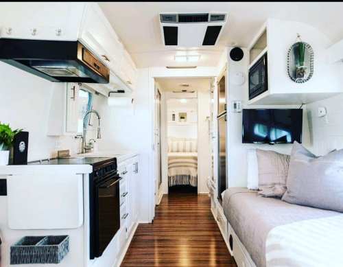 A modern, compact RV interior featuring a kitchen, living area, and cozy sleeping space with light wood accents.