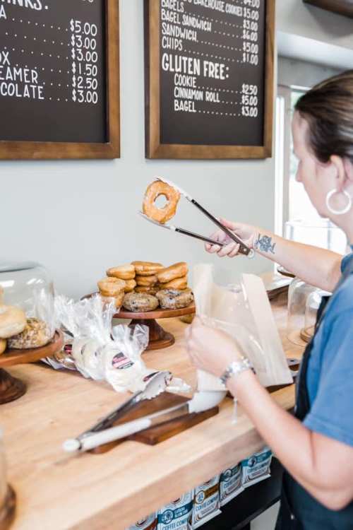 A person using tongs to pick up a donut from a display of baked goods on a wooden counter.