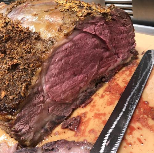 A close-up of a roasted beef joint with a crispy crust, resting on a cutting board with juices around it.