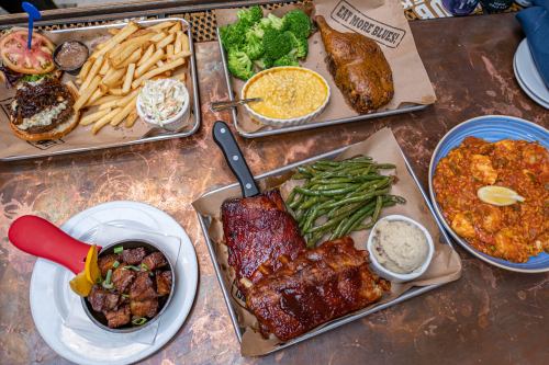 A spread of hearty dishes including ribs, fries, broccoli, mac and cheese, and a burger on a copper table.