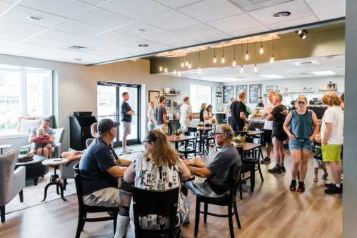 A busy café interior with people socializing, sitting at tables, and ordering at the counter. Bright and inviting atmosphere.