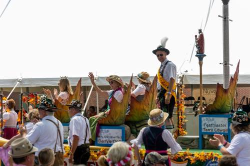 A festive parade float with people in traditional attire, waving to the crowd, surrounded by colorful decorations.