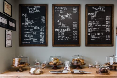 A cozy café display with a menu board and a variety of baked goods under glass cloches on a wooden counter.