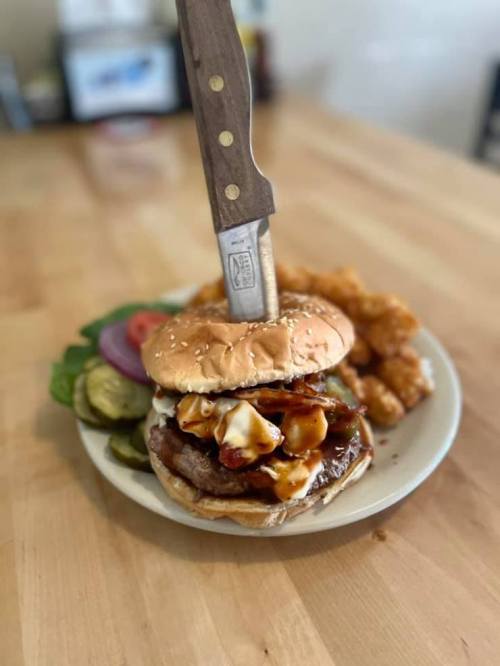 A burger with a knife stuck in it, served with pickles, lettuce, tomato, and chicken tenders on the side.
