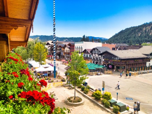 A vibrant street scene in a charming town, featuring colorful buildings, flowers, and mountains in the background.