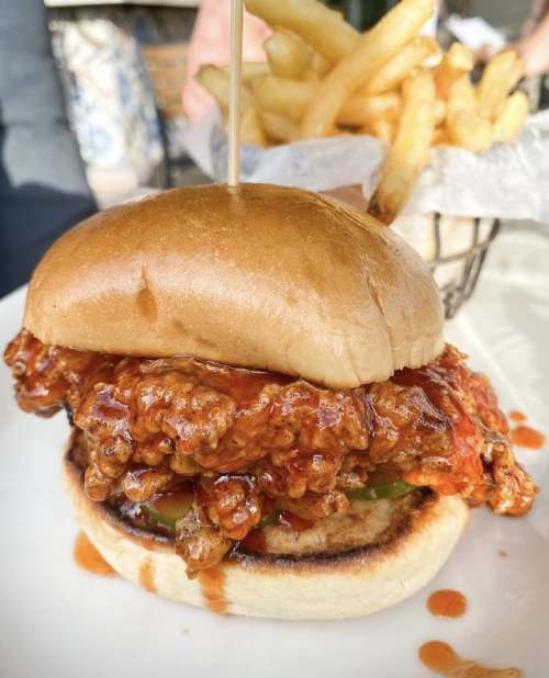 A crispy fried chicken sandwich with spicy sauce, lettuce, and a soft bun, served with a side of French fries.