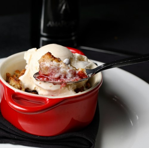 A red dish with a scoop of ice cream on top of a warm dessert, with a spoonful of the dessert lifted above.