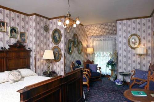 Cozy vintage bedroom with floral wallpaper, antique furniture, and framed portraits on the walls. Soft lighting creates warmth.