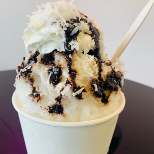 A cup of shaved ice topped with whipped cream, chocolate syrup, and shredded coconut.