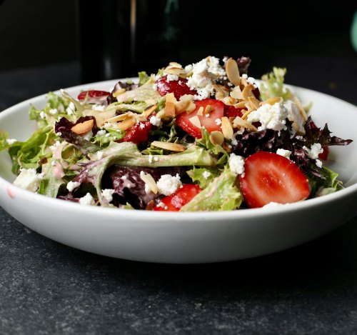 A fresh salad with mixed greens, sliced strawberries, almonds, and crumbled cheese in a white bowl.