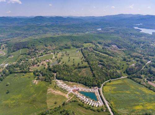Aerial view of lush green hills, a lake, and a residential area with a pool surrounded by trees and fields.