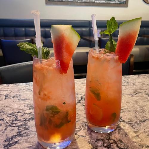 Two refreshing watermelon cocktails with mint leaves, served in tall glasses on a marble table.
