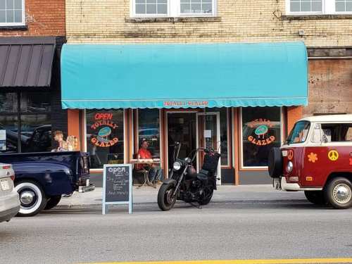 A colorful storefront with a turquoise awning, a motorcycle parked outside, and a vintage van nearby.