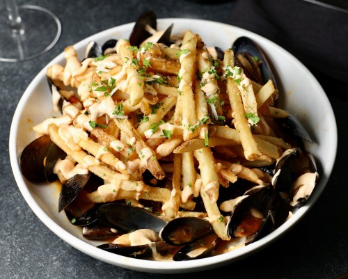 A bowl of fries topped with mussels and drizzled with sauce, garnished with chopped herbs.