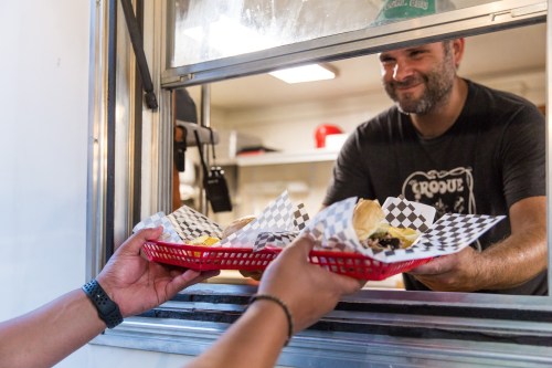 A food truck worker hands a tray of food to a customer through a service window.