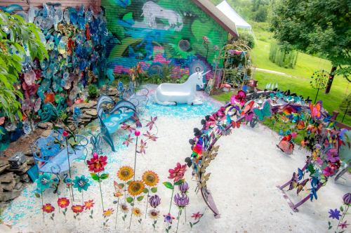 A colorful garden with whimsical metal flowers, a white unicorn statue, and vibrant murals on the walls.
